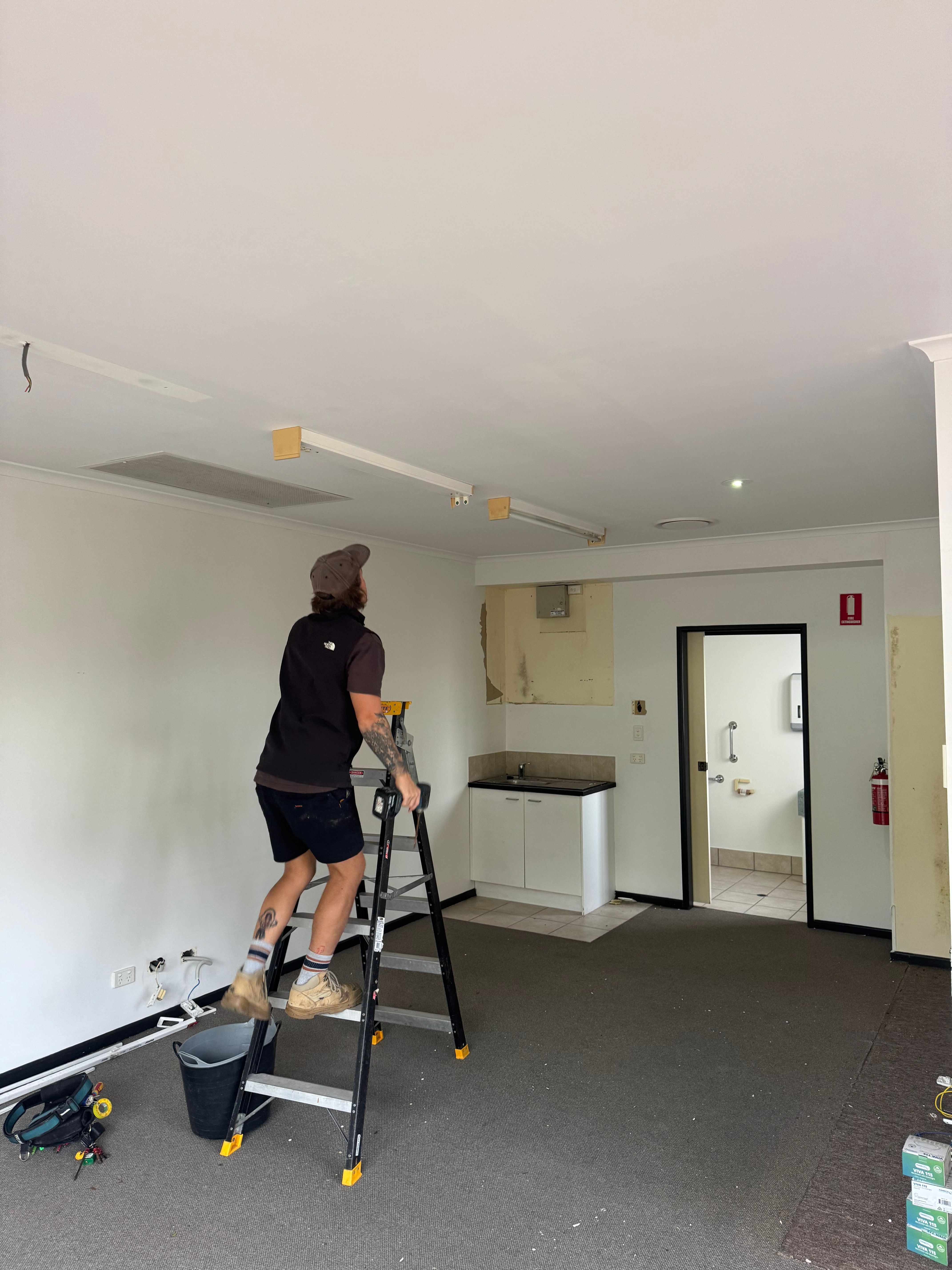 Electrician on ladder preparing to remove fluorescent battens