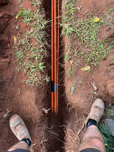 Orange sub-main conduits laid in a narrow trench in red soil