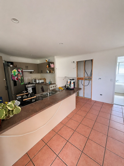 Original kitchen and dining layout before renovation, featuring outdated cabinetry, tiled flooring, and exposed electrical rough-in work during construction.