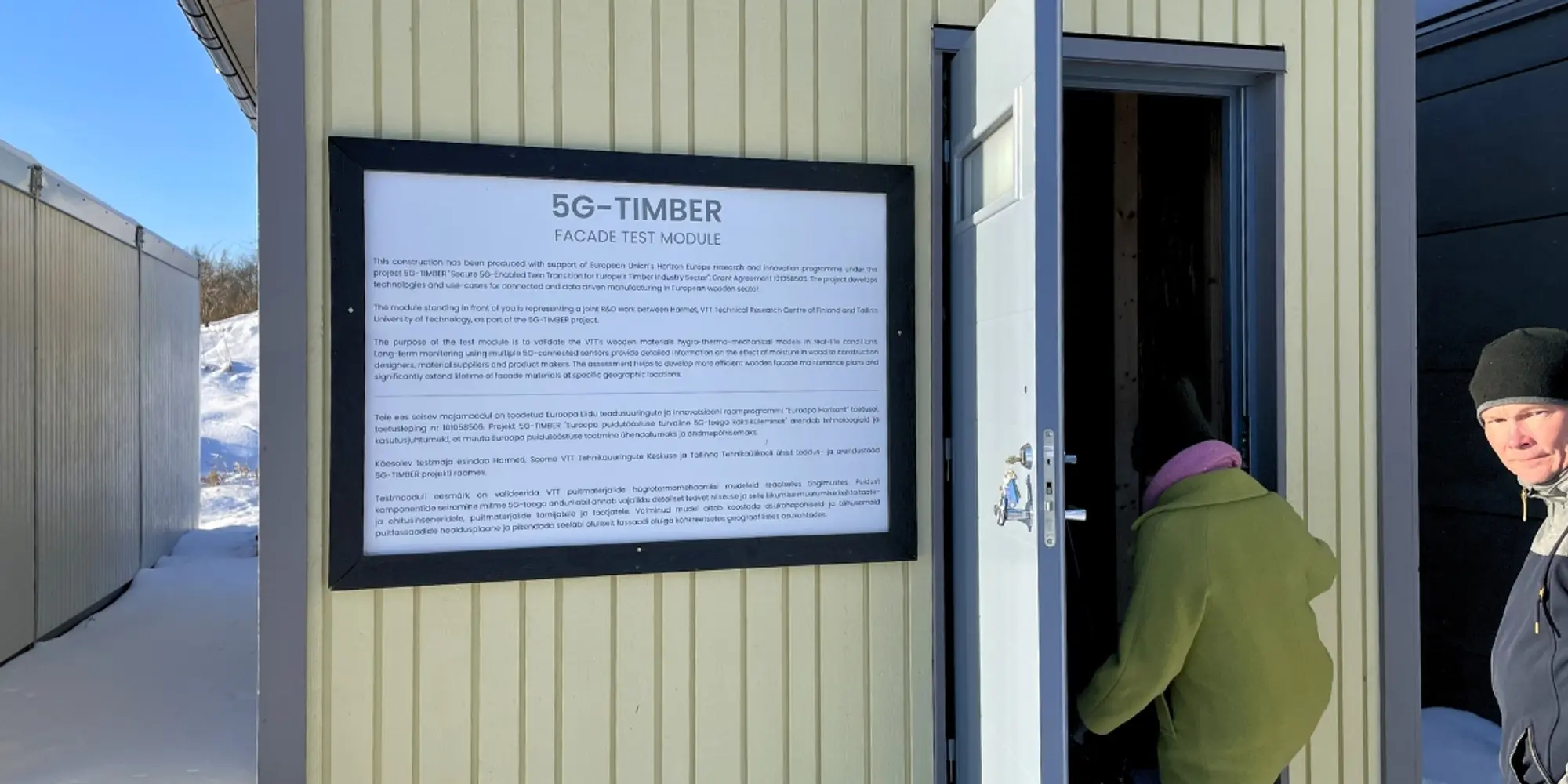 Entrance to the 5G-TIMBER experimental module with information panel and people entering.