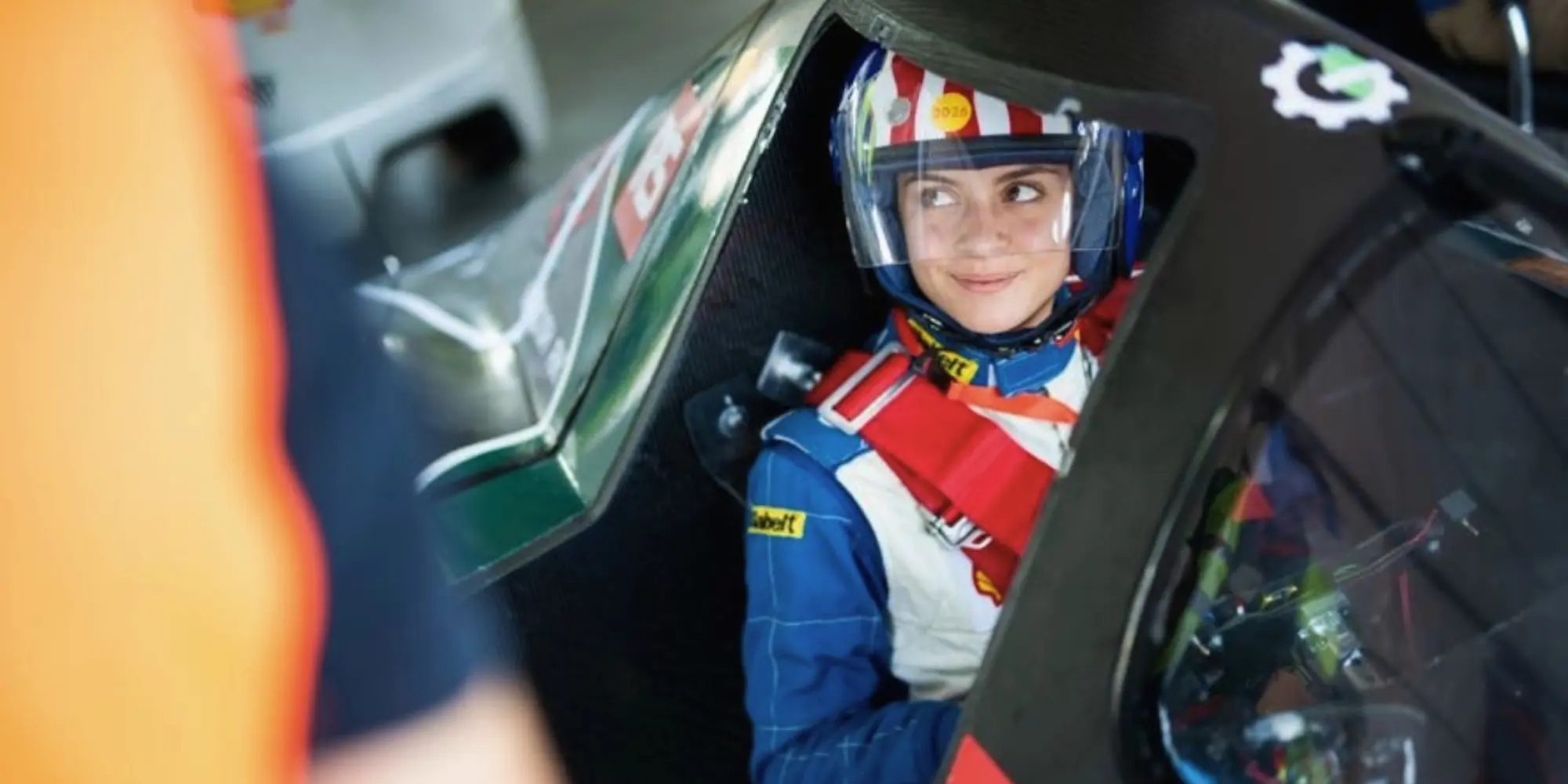 Driver wearing a helmet and safety harness inside an experimental vehicle cockpit.