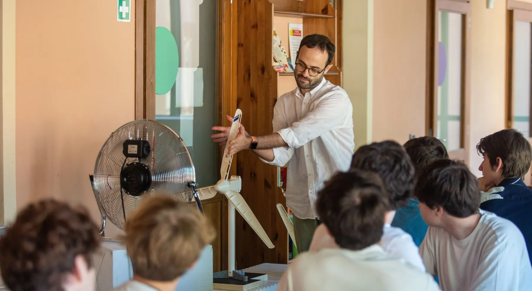 Docente mostra un modello di turbina eolica a un gruppo di studenti durante una lezione pratica.