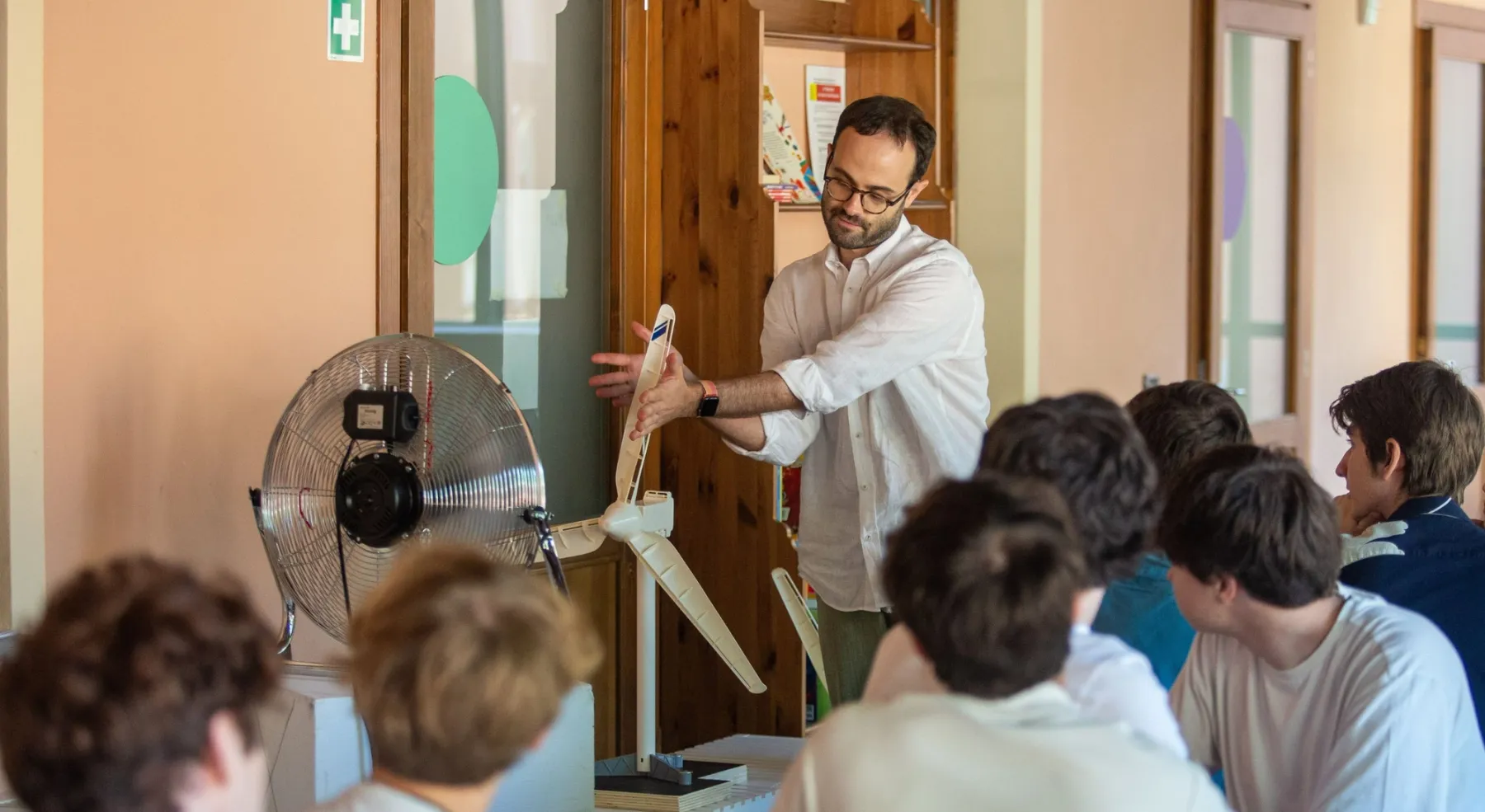 Docente mostra un modello di turbina eolica a un gruppo di studenti durante una lezione pratica.