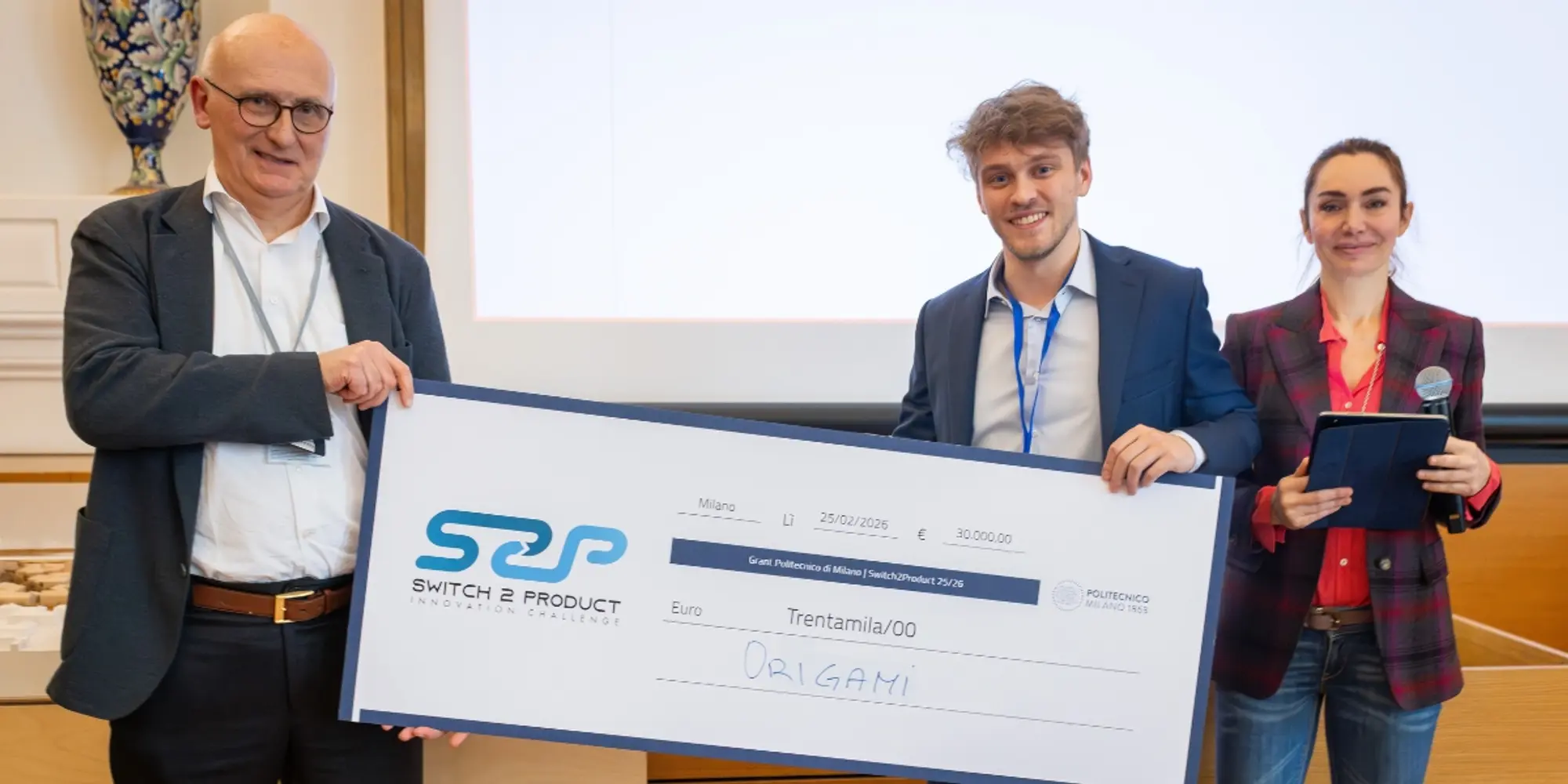 Three people holding a symbolic check for the Origami project during an award presentation.