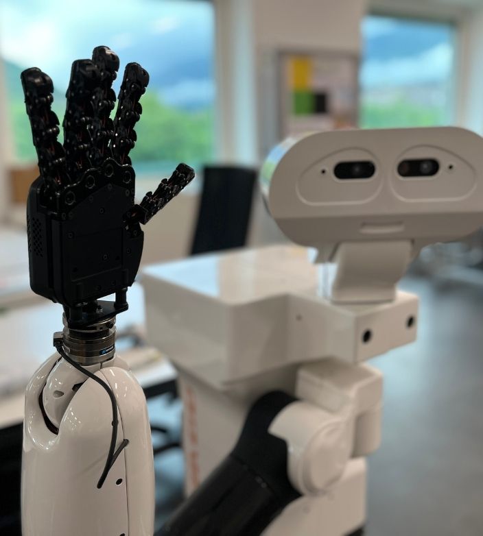 Mano robotica articolata accanto a un robot umanoide in un laboratorio.