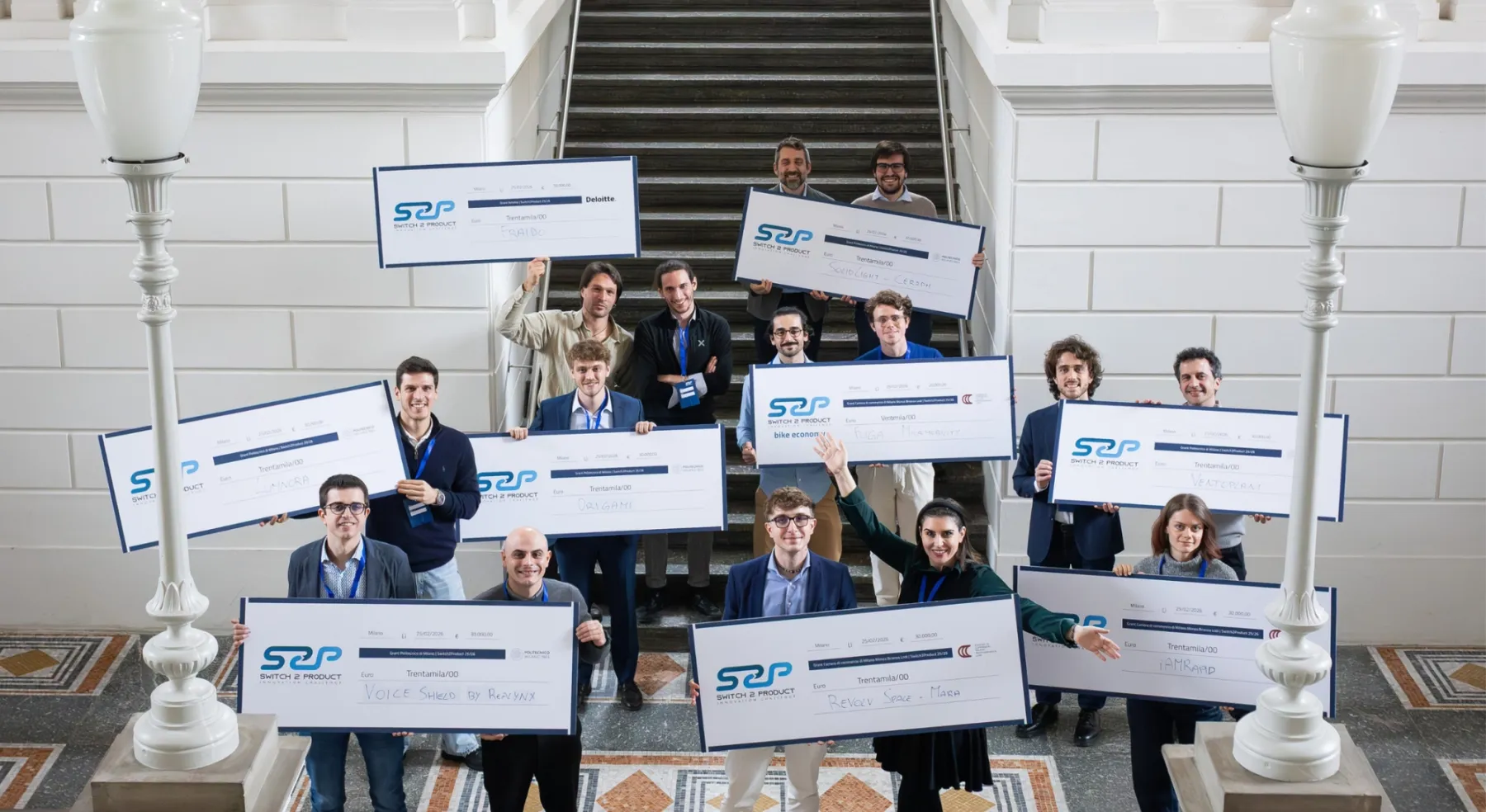Group of people on a staircase holding large checks during an award ceremony.