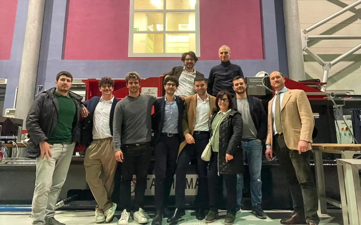 Gruppo di persone in posa davanti a macchinari in un laboratorio industriale.