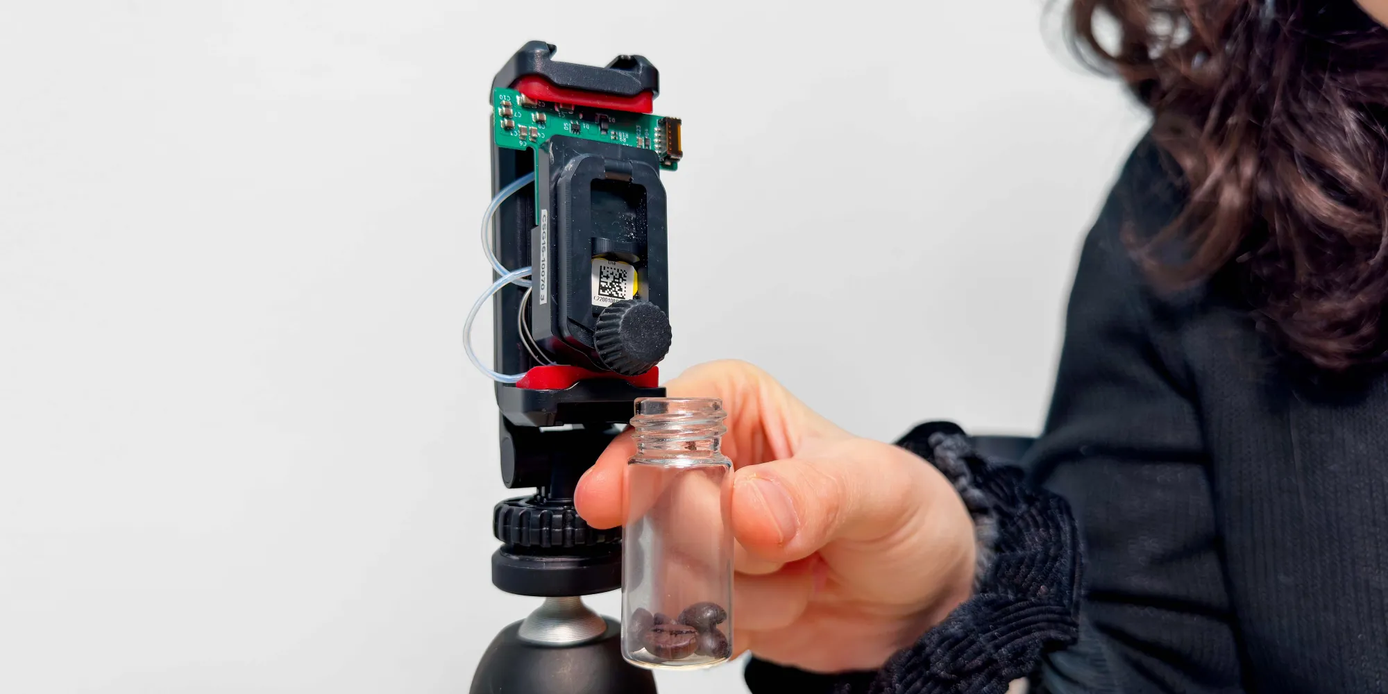Close-up of a transparent container with a sample in front of a technological device on a tripod.