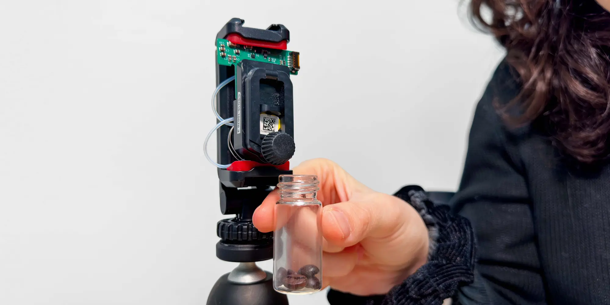 Close-up of a transparent container with a sample in front of a technological device on a tripod.
