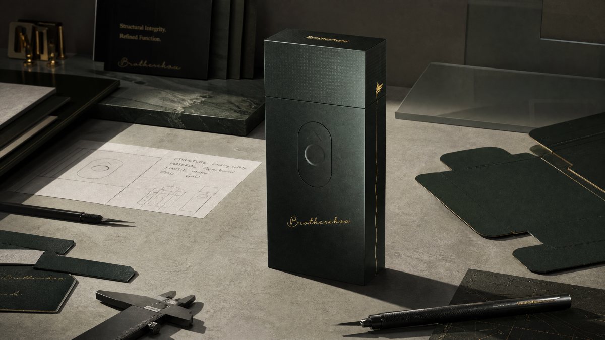Matte black cigarette case on a desk with drafting tools and die-cut drawings.