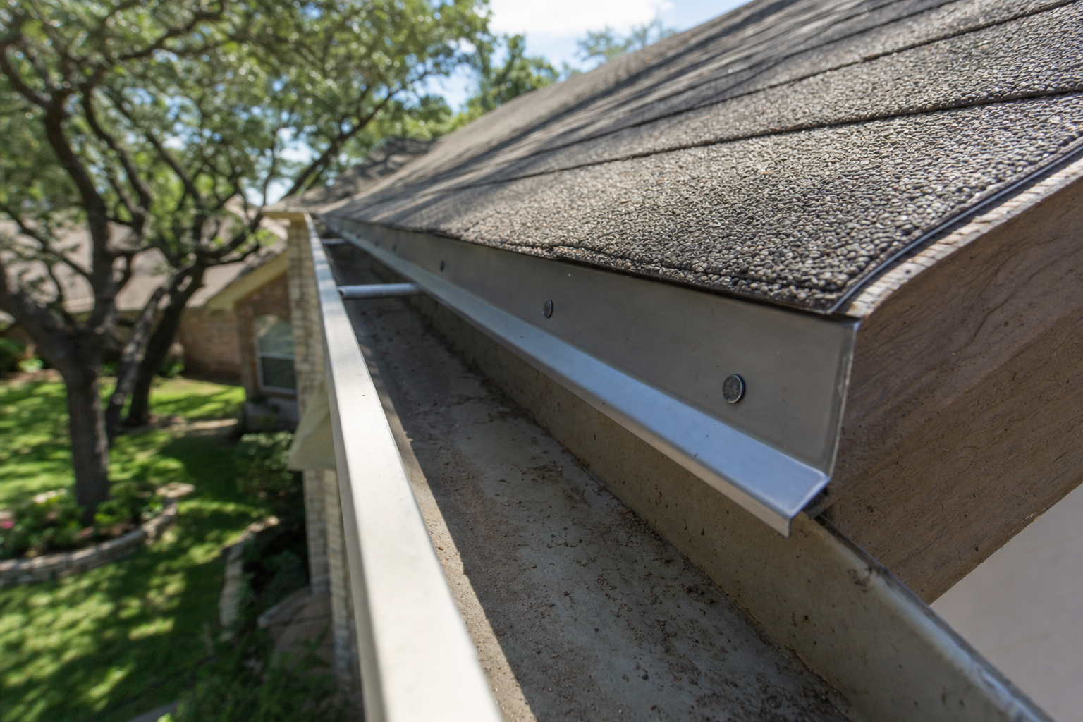 Close-up of metal drip edge flashing installed under shingles at a roof eave directing water into the gutter.