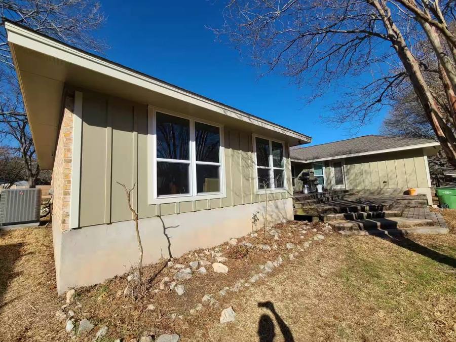A renovated ranch-style home featuring earth-tone board and batten siding paired with new energy-efficient white vinyl windows.