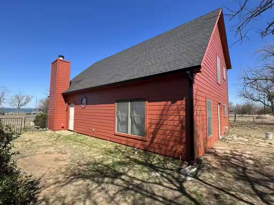 A striking exterior transformation featuring bold red James Hardie lap siding installed on a steep-pitched home near the water. The project highlights clean lines, a sided chimney chase, and dark contrasting roof shingles.