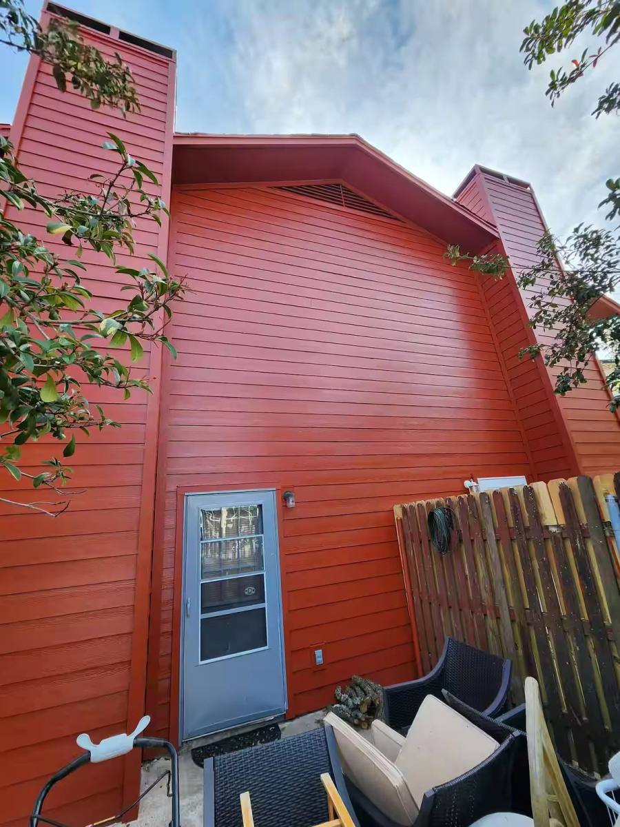 A low-angle view of a multi-story residential exterior featuring vibrant terracotta horizontal lap siding and a chimney chase.