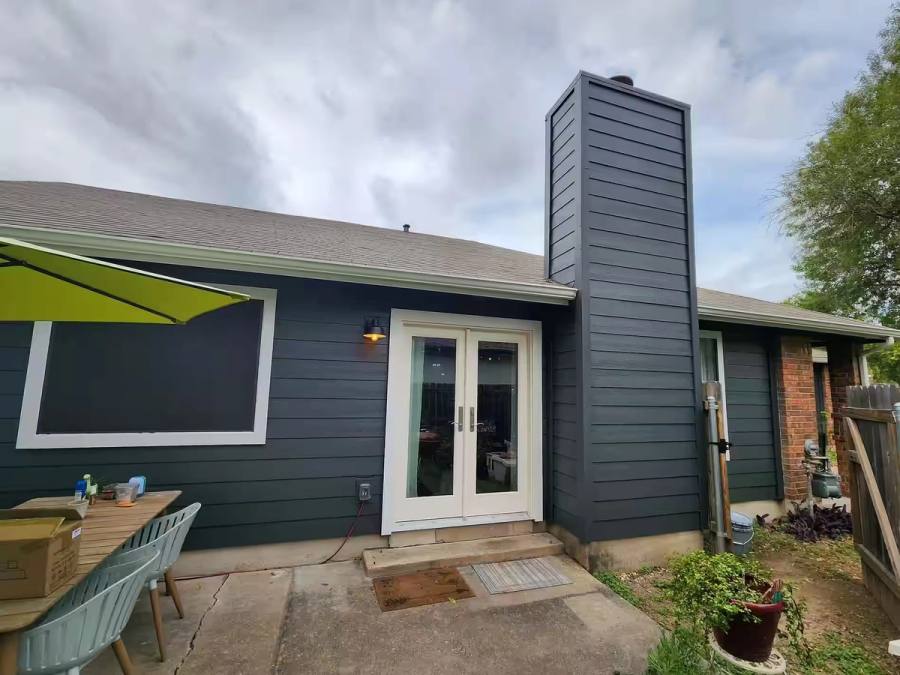 A backyard exterior renovation featuring dark gray James Hardie siding installed on the rear wall and chimney, complemented by white French doors.