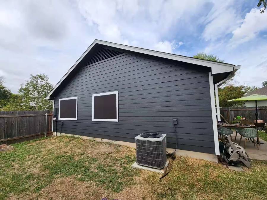 Side profile of a home featuring newly installed dark gray fiber cement lap siding with contrasting white trim. Highlights the clean lines of the gable end and professional installation around windows and vents.