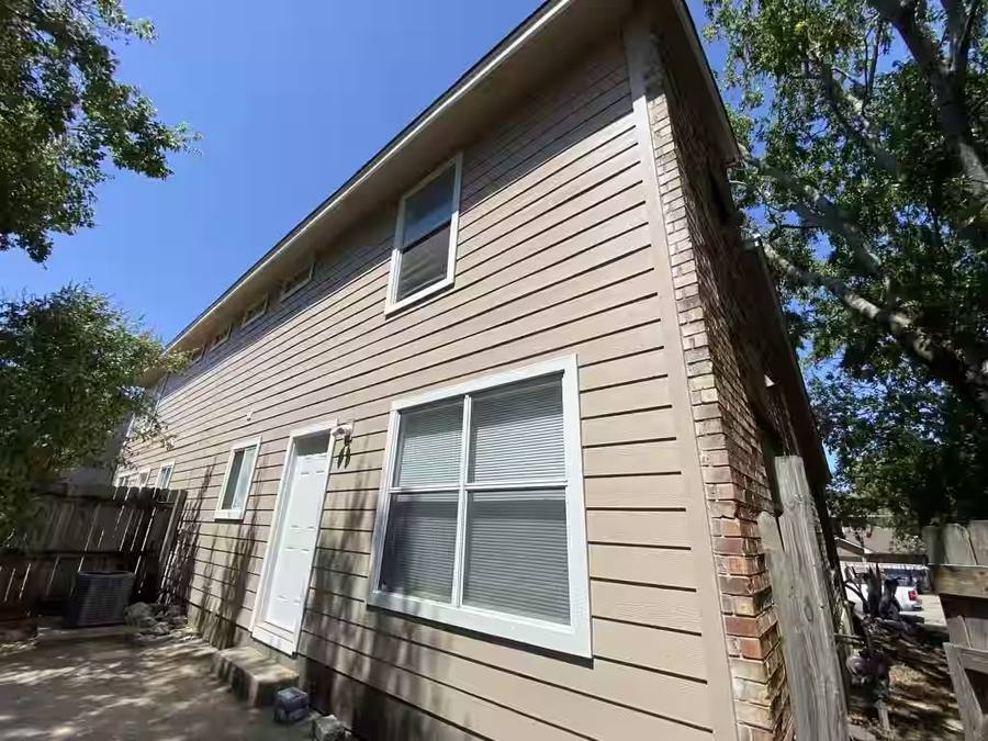 Side elevation of a two-story home featuring tan horizontal lap siding and white vinyl windows. The clean exterior renovation highlights the durability of modern fiber cement materials.