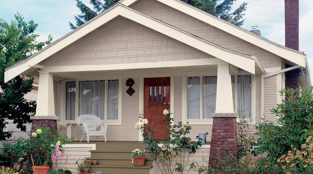 Craftsman bungalow in a pale neutral with a red front door and brick porch piers, from Sherwin-Williams’ exterior color gallery