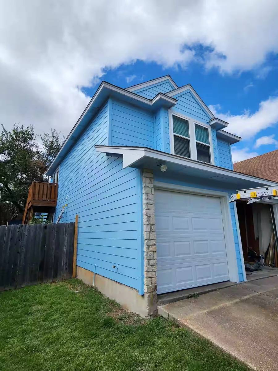A renovated two-story detached garage featuring vibrant blue fiber cement lap siding, white trim, and a limestone corner accent.