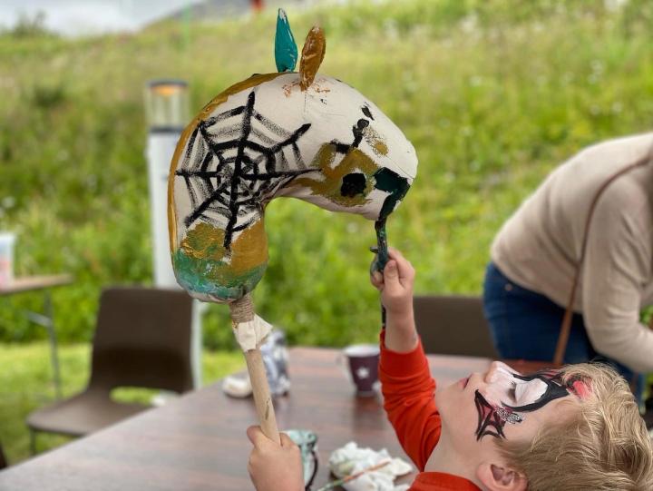 Et barn med ansiktsmaling holder opp en selvlaget kjepphest av papp på en barnefestival.