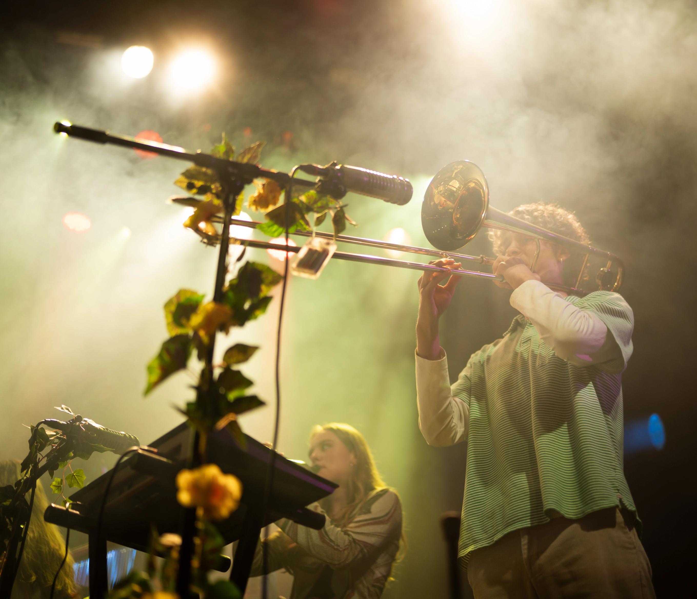En mann i grønn skjorte spille trombone på en lyssatt scene