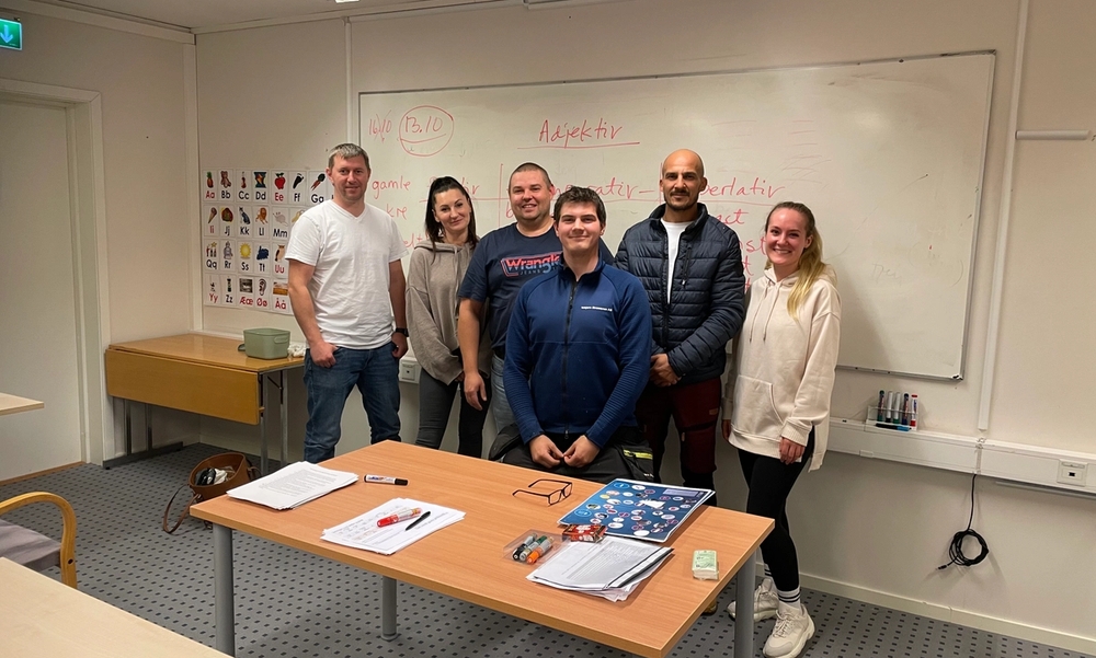 Personer står oppstilt foran tavle.