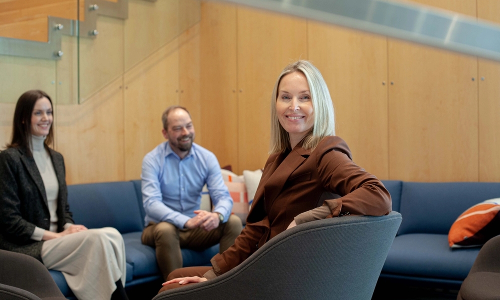 Tre personer i en sittegruppe. Ene personen smiler inn i kamera.