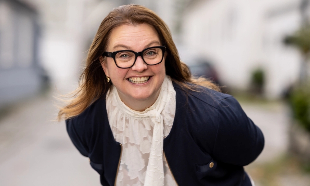Kvinne med briller lener seg fremover og smiler til kamera