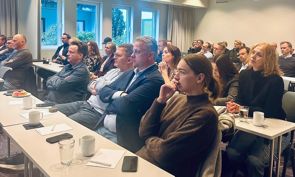 Publikum sitter ved skrivepulter på rekke og rad