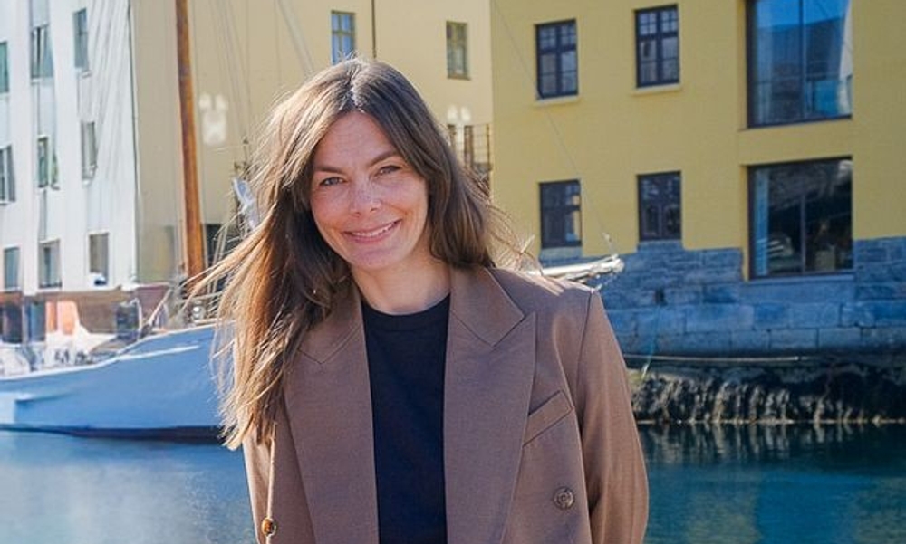 Kvinne står med sjø og gule jugendbygg i ryggen.