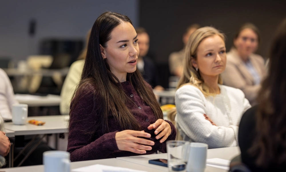 To kvinner på forelesning, kaffekopper på bordet.