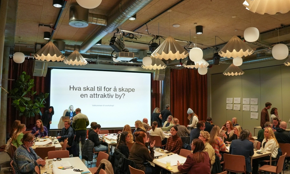 deltakere i en sal på en konferanse med en stor skjerm i bakgrunnen
