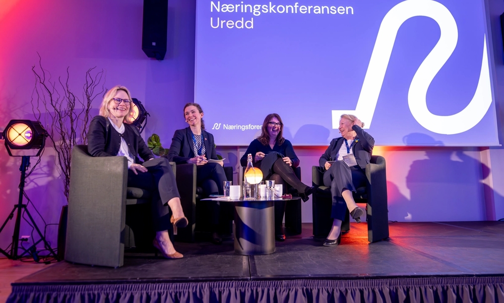 Personer sitter i panelsamtale på en scene og smiler og ler