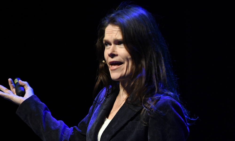 Kvinne i sort dress på en scene med klikker i hånden.