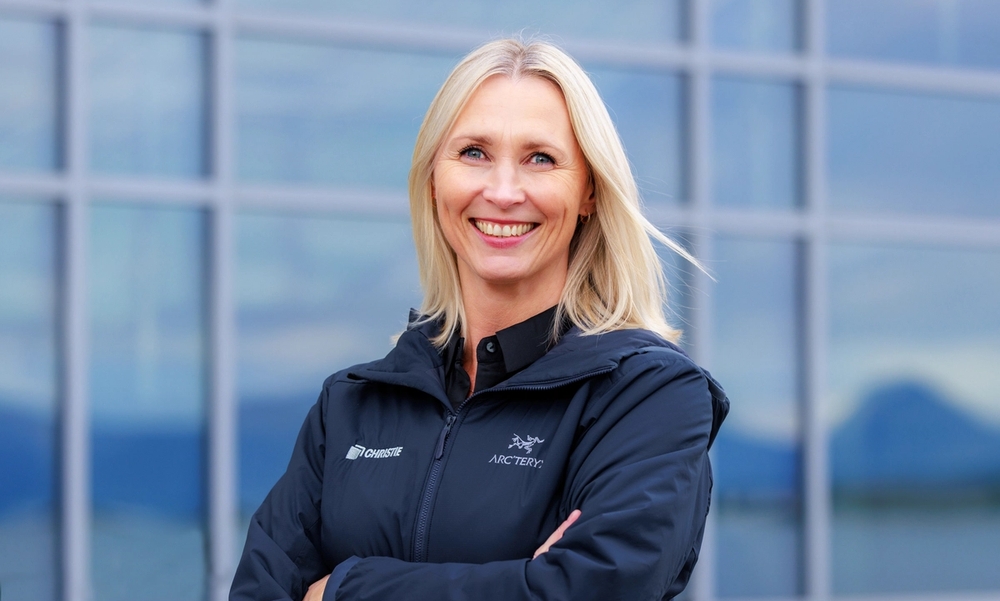 Kvinne foran bygg med speilvinduer med sporty jakke og armene i kors