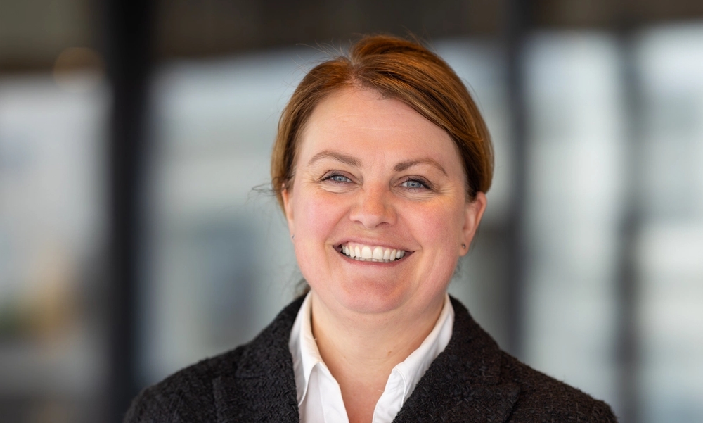 Kvinne i sort dressjakke og hvit skjorte smiler