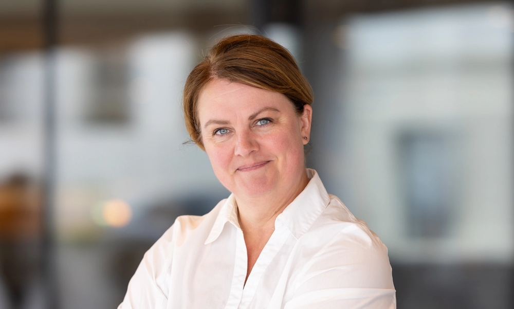 Kvinne i hvit skjorte smiler inn i kamera