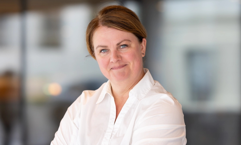 Kvinne med armene i kors i hvit skjorte smiler