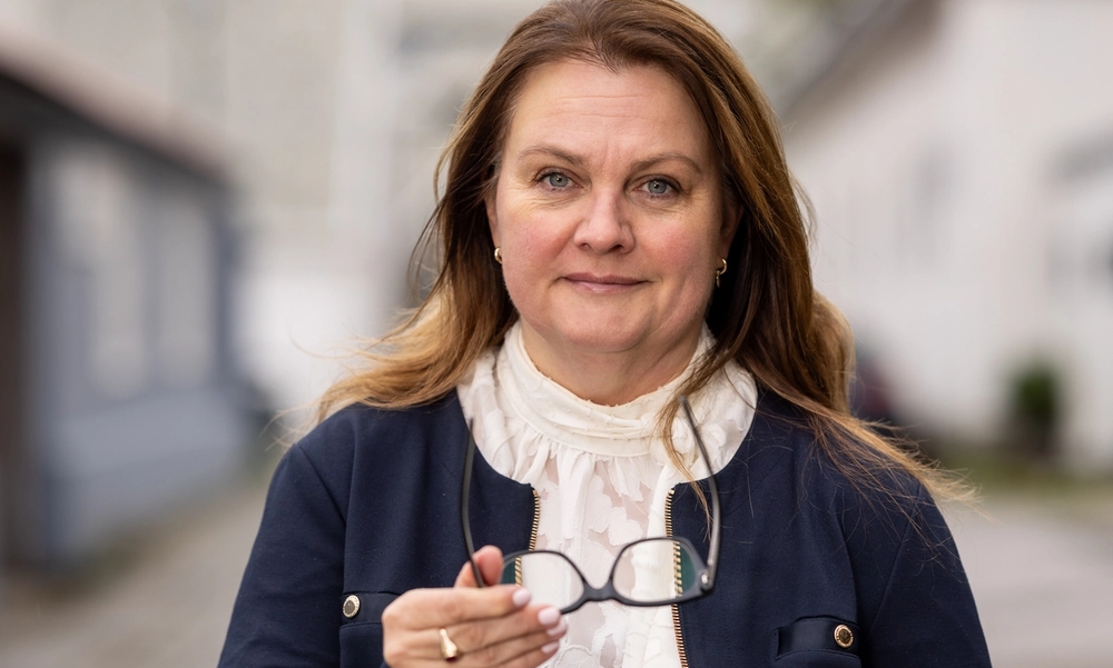 kvinne i hvit bluse og blå dressjakke med brillene i hånden