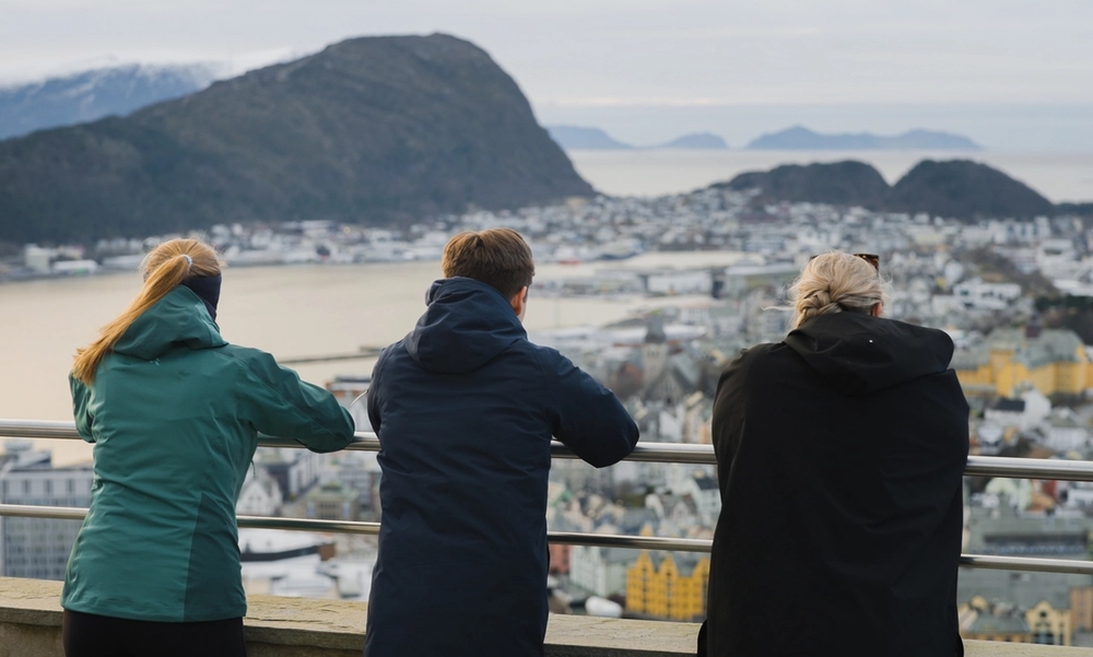 Tre ungdommer som ser utover en by fra et utsiktspunkt med ryggen til kamera.
