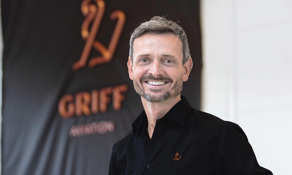 mann med skjegg i sort skjorte som smiler mot kamera