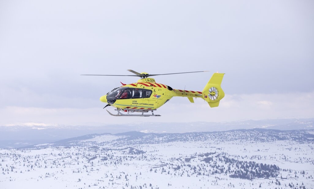 Gult ambulansefly i lufta over snøkledd landskap