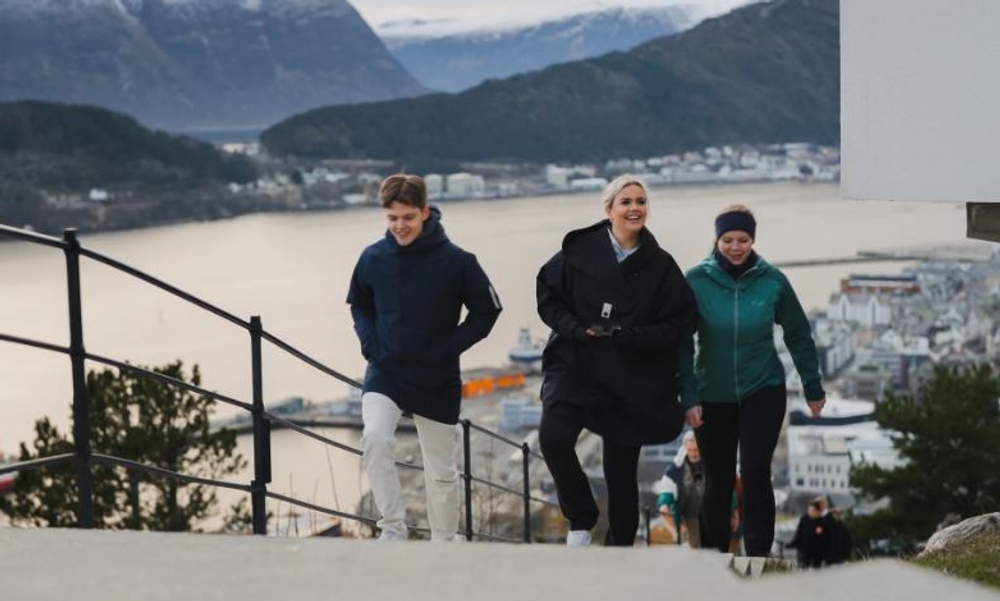 Tre unge personer går opp trappene til utkikkspunkt med by i bakgrunnen