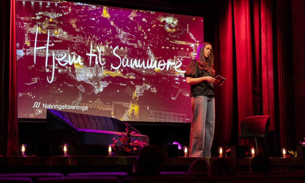 Kvinne står på en scene med en plakat i bakgrunnen