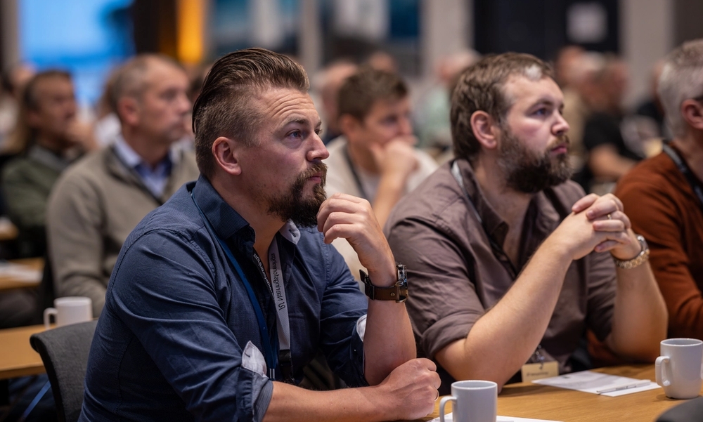 To menn sitter på konferanse og lytter