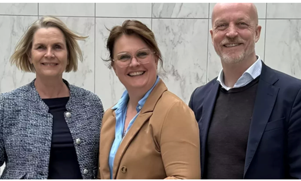 Tre personer i dressjakker smiler