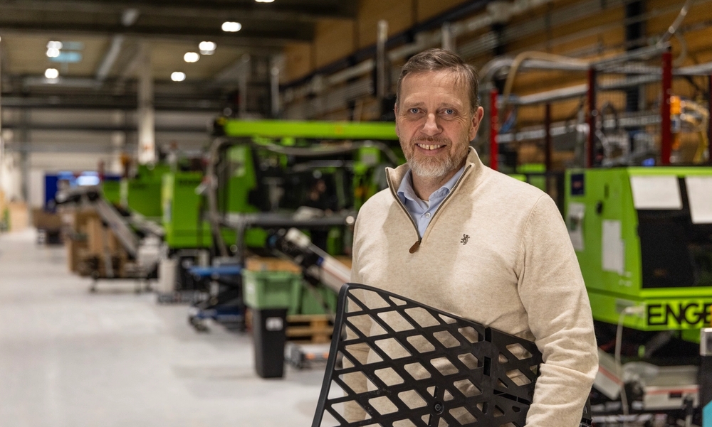 Mann står i en produksjonshall med et sort plastgitter under armen.