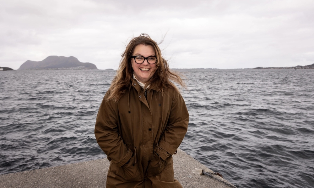 Kvinne står på en molo med havet i bakgrunnen og vind i håret