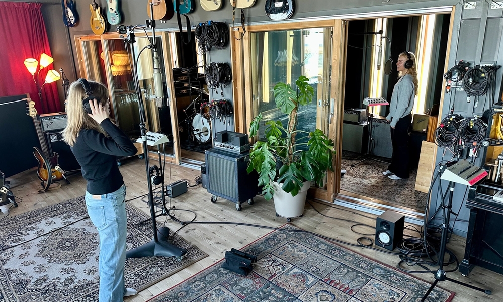 To kvinner står i studio med headset og synger inn i mikrofon