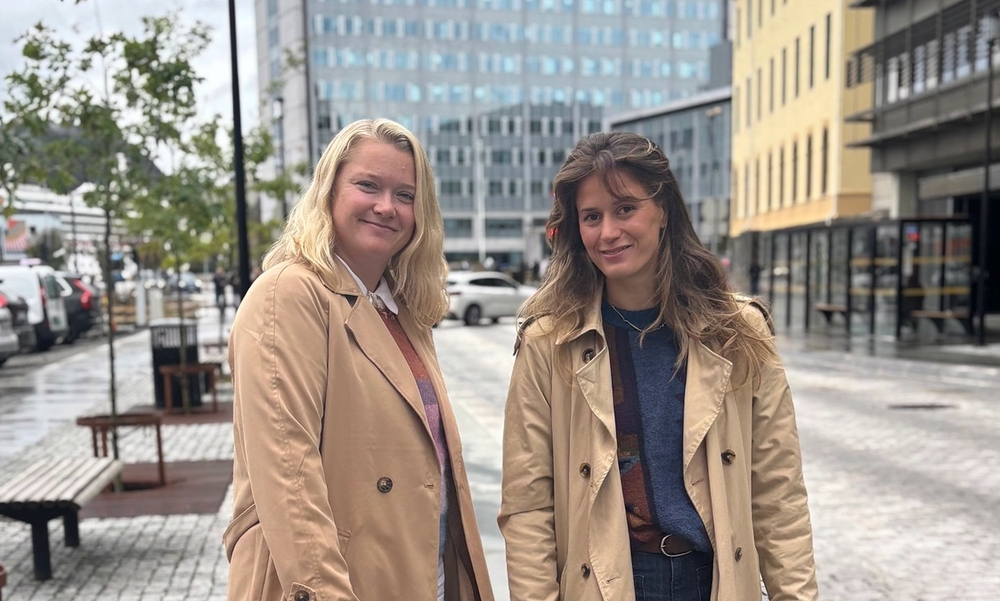 To kvinner i beige trenchcoat står i en bygate